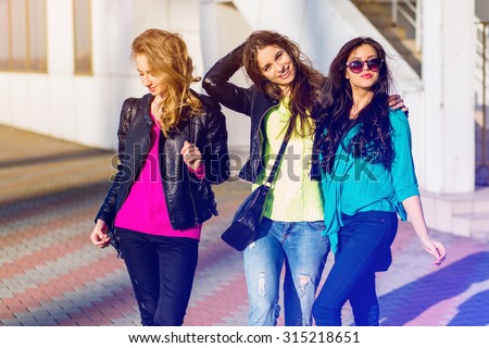 Three best friends have fun on sunny autumn day urban street background .  Group of  students walking, wearing color fall sweater  and leather jacket. Bright colors.