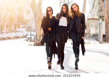 Three pretty  young girls having fun outdoors together . Lifestyle urban mood.  Center city background. Best friends wearing black casual outfit.