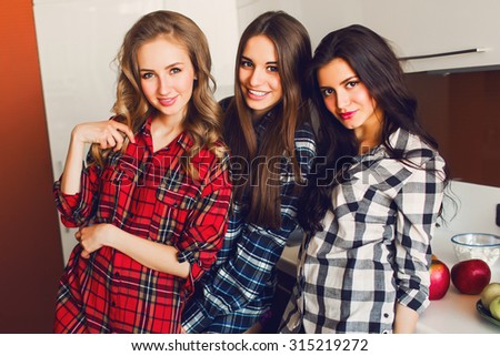 Close up indoor lifestyle portrait of three funny young friends have fun and pretending faces on the kitchen . Home party mood. Wearing plaid shirt. Warm soft photo.