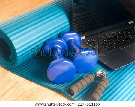 Getting in shape with online training at home. Computer, dumbbells and a handgrip on a yoga mat to work out online. Home gym, body care, healthy lifestyle, remote exercise, sports concept. Foto stock © 