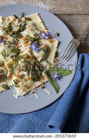 italian handmade pasta ravioli with borage herb, flower, sage, crisp onion on plate on rustic wooden table