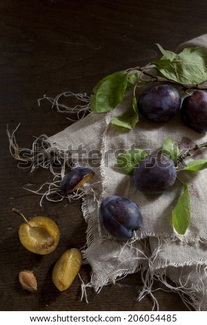 whole and slice prunes with leafs on rustic background with jute napkin