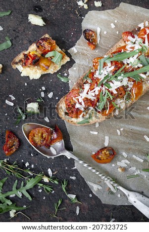 italian bruschetta with baked cherry tomatoes, parmesan cheese and rocket on toasted slice of bread