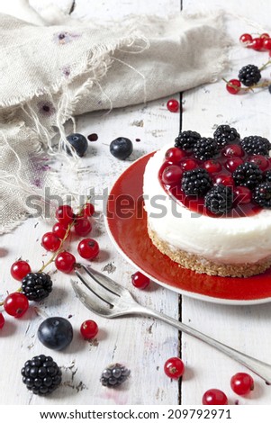 whole mini cheesecake with blackberries, blueberries and red currant on plate with fork and berries on wooden white table