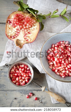 half pomegranate with branch and grains on bowl on wooden rustic table with vintage strainer full of grains and napkin