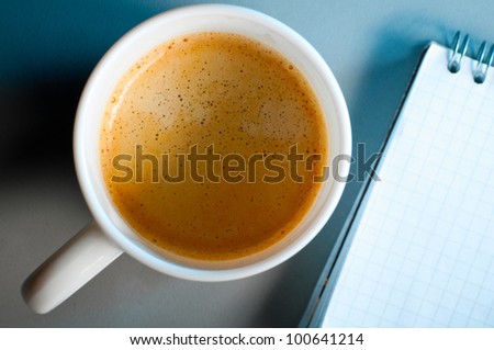 cup of coffee and notebook on table in blue light. Focus on mug