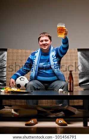 soccer fan is sitting on sofa with beer at home