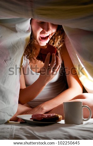 woman is sitting under cover in bed and eating