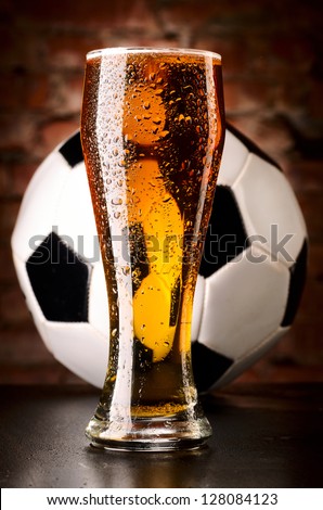 glass of lager with soccer ball on table against brick wall