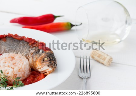Steamed sea bass in tomato sauce with chili pepper and glass of white wine on white table.
