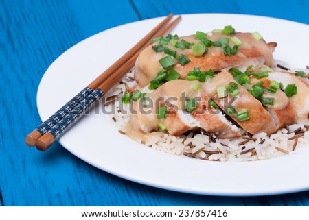Chicken fillet served with miso sauce and rice on white plate. Wooden chopsticks. Blue wooden background.