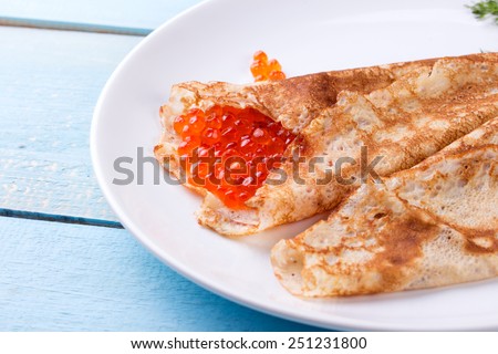 Pancake day, mardi gras, maslenitsa background. Thin rolled pancakes, crepes with red caviar. Traditional Russian dish.
