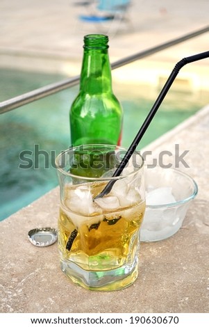 Glass of cold beer with ice cubes near a swimming pool