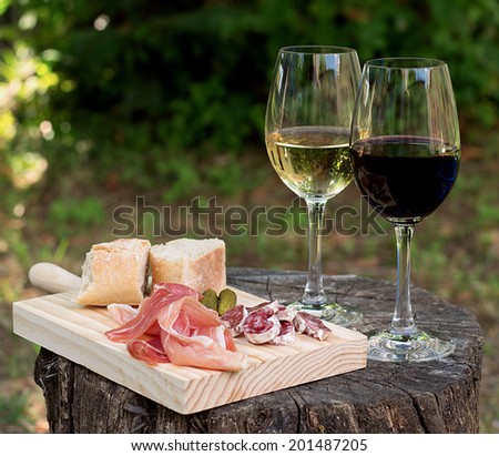 Red and white wine in a glass with sausage, ham in the nature. Selective focus on the wine