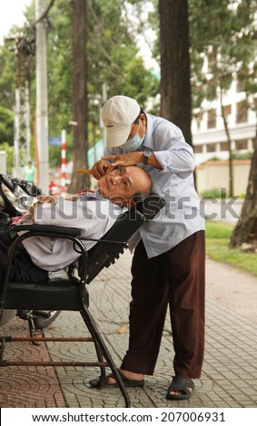SAIGON, VIETNAM - JUL 15, 2014: Unidentified old hairdresser serving an old man on street in Saigon, Vietnam. July, 15, 2014