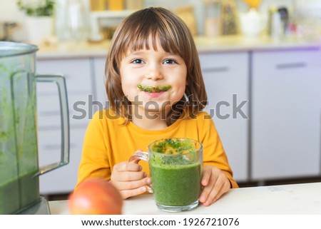 Happy Kid with glass cup of green smoothies in hands. Cute boy crazy drinks healthy dietary nutritious cocktail at home in the kitchen. Healthy lifestyle, raw food