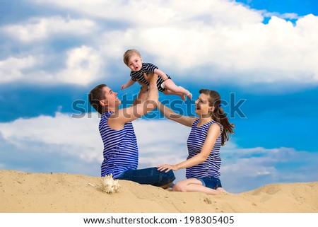 Happy family, mom, dad and little son in striped vests having fun  in the sand outdoors against blue sky background. Summer vacations concept.