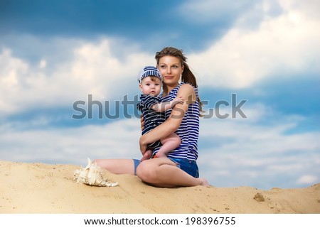 Happy family, mom and little son in striped vests having fun  in the sand outdoors against blue sky background. Summer vacations concept.