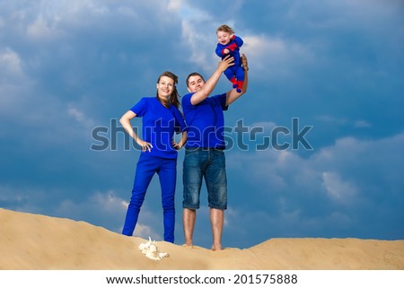 Happy family, mom, dad and little son having fun  in the sand outdoors against blue sky background. Summer vacations concept.