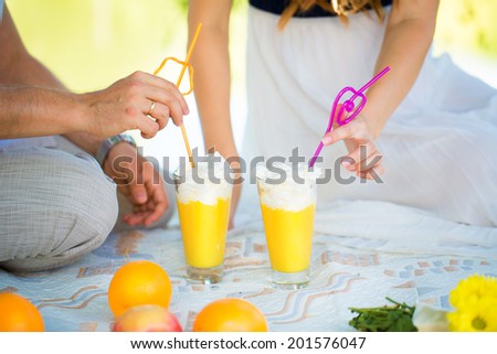 Women\'s and men\'s hands with wedding rings. Picnic in the nature. The glasses of orange juice and whipped cream. Summer vacation concept.