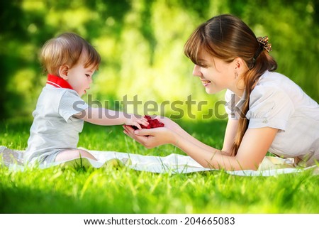 Happy family, mom and little son having fun in the park. Raspberry in his hands. Summer vacations concept.