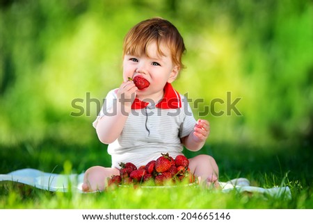 Happy baby have fun in the Park on a Sunny meadow with strawberry. Summer vacation concept. The emotions.