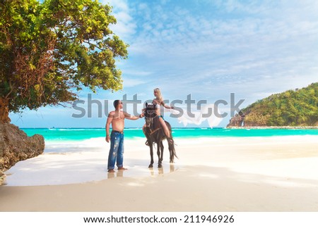 Young couple in love walking with the horse on a tropical beach. Tropical sea in the background. Summer vacation.
