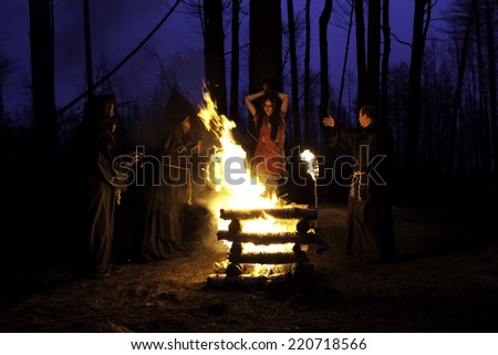 Scary Halloween photo. Men in black clothes, burn the witch at the stake at night in the forest.