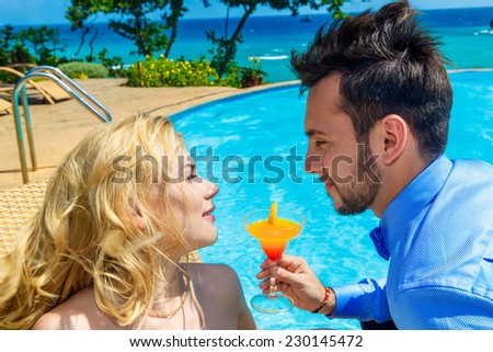 happy bride and groom enjoy a cocktail poolside infinity. Tropical sea in the background.
