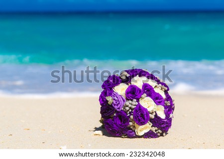 Wedding bouquet lying on the sand on a tropical beach. Blue sea in the background.