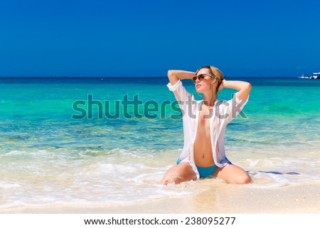 Young beautiful girl in wet white shirt  on the beach. Blue tropical sea in the background.