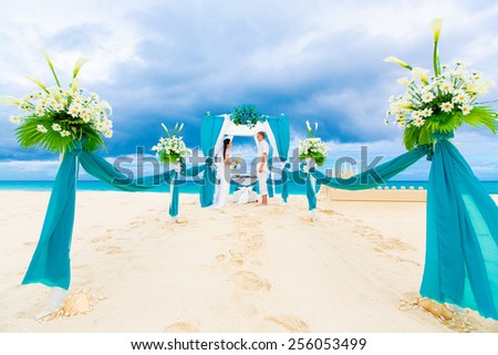 Wedding ceremony on a tropical beach in blue. Happy groom and bride under the arch decorated with flowers on the sandy beach. Wedding and honeymoon concept.