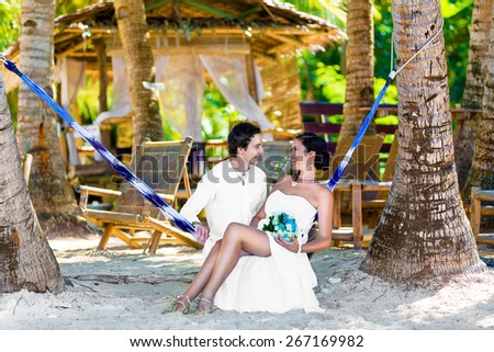 Happy bride and groom having fun in a hammock on a tropical beach under the palm trees. Summer vacation concept.