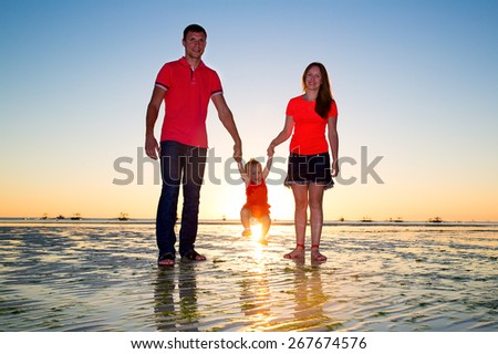 Happy family, mom, dad and little child having fun on a tropical beach at sunset. Summer vacation concept. Outdoor portrait of a happy family.