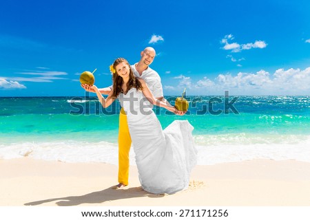 Happy bride and groom drink coconut water on a tropical beach. Wedding and honeymoon on the tropical island.