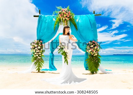 Wedding ceremony on a tropical beach. Happy bride under the wedding arch  decorated with flowers on tropical sand beach. Wedding and honeymoon concept.