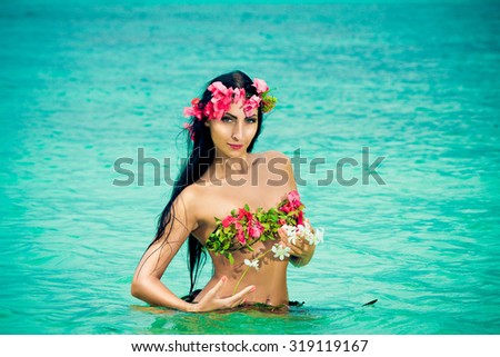 Young beautiful girl in a bikini made of flowers in the tropical sea.