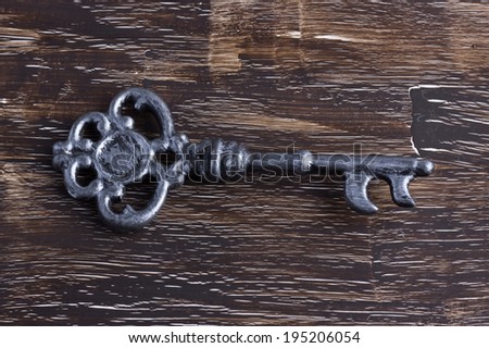 Single silver antique key on wooden background