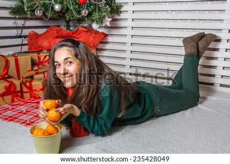 Beautiful and happy girl with gifts near a Christmas tree wishes everyone a Merry Christmas and Happy New year with tangerines