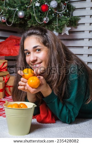 Beautiful and happy girl with gifts near a Christmas tree wishes everyone a Merry Christmas and Happy New year with tangerines