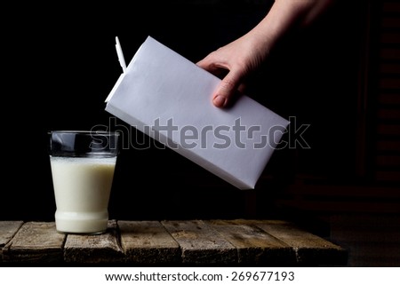 Female hand holding a carton of milk and pour into a glass on a wooden vintage background