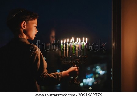 The child lights the menorah for Hanukkah on the windowsill. The boy in the kippah sitting by the window. Jewish holiday. Tradition is a religious ritual. Sunset. The first star. Judaism Foto stock © 