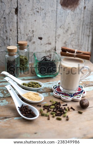 glass of hot indian yoga drink - masala chai tea with spices and igredients on a rustic table