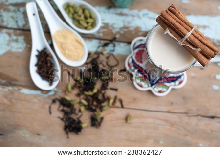 glass of hot indian yoga drink - masala chai tea with spices and igredients on a rustic table