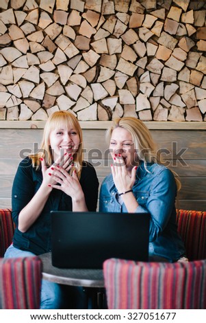 Two beautiful blond girls working on the laptop in coffee bar.