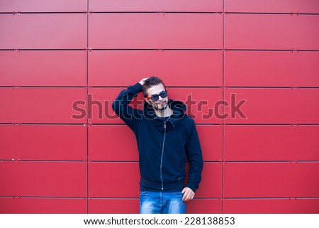 Young model making strange faces on red background, wearing purple sunglasses
