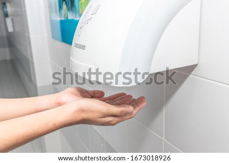 Automatic hand dryer in public toilet or restroom hygiene concept. A man hands using utomatic hand dryer in bathroom.