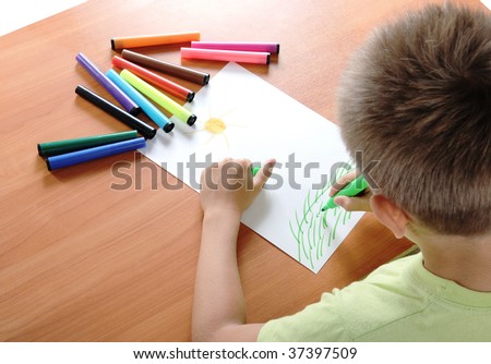 child draws green grass and sun on white paper by colour pensil