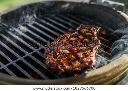 Premium dry-aged rib-eye steak grilling on a kamado grill. Dry-aged raw meat steak grilling and smoking on direct fire. Perfect grill marks, and golden crust on the grilled meat. Grilling rib eye