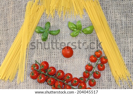 Italian spaghetti pasta with cherry tomatoes and basil, in a funny cute face shape, on natural jute sackcloth background.Genuine mediterranean diet.